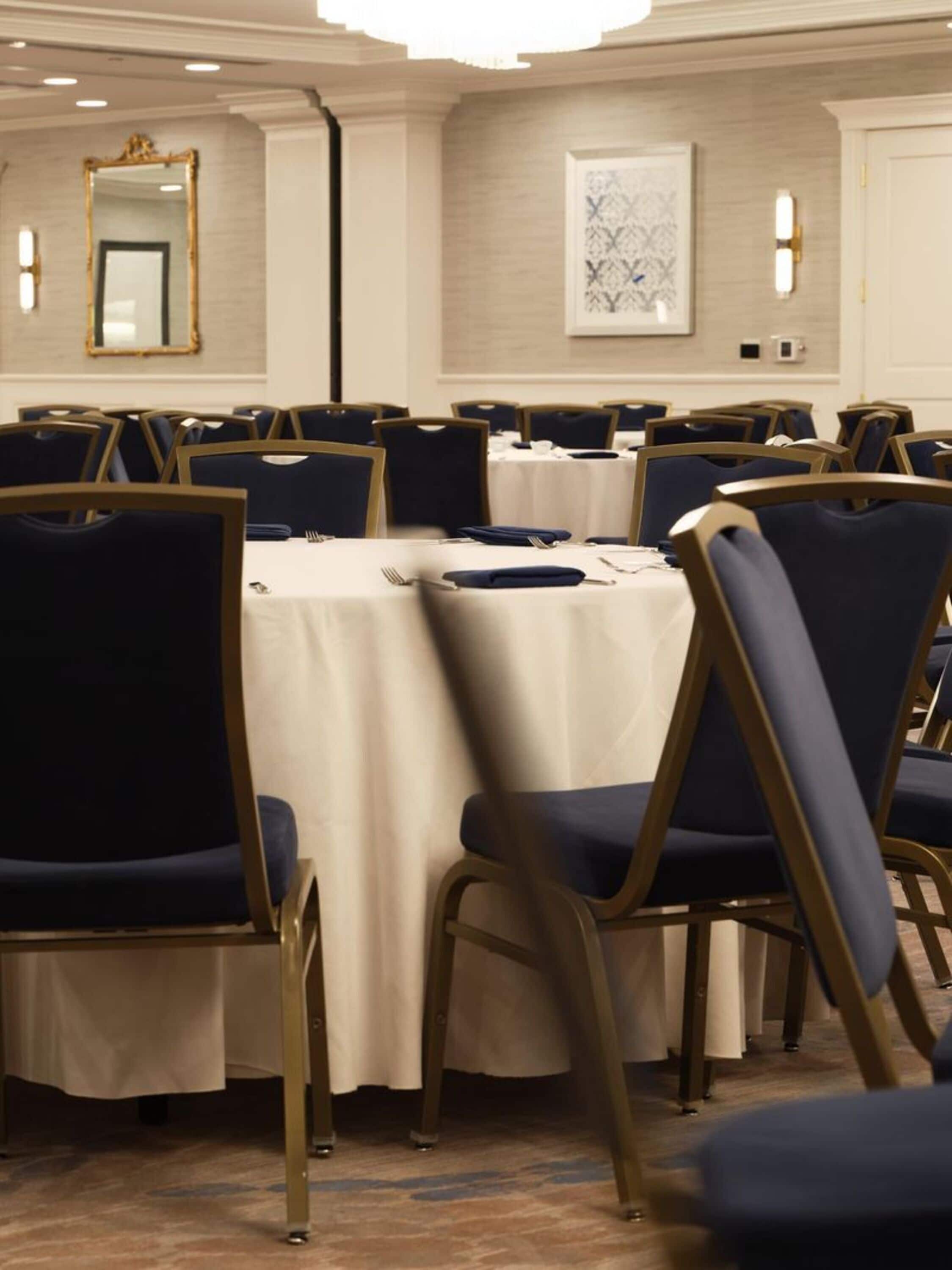 Une salle de conférence dotée de tables rondes, de chaises rembourrées bleues et d’une décoration aux couleurs neutres.