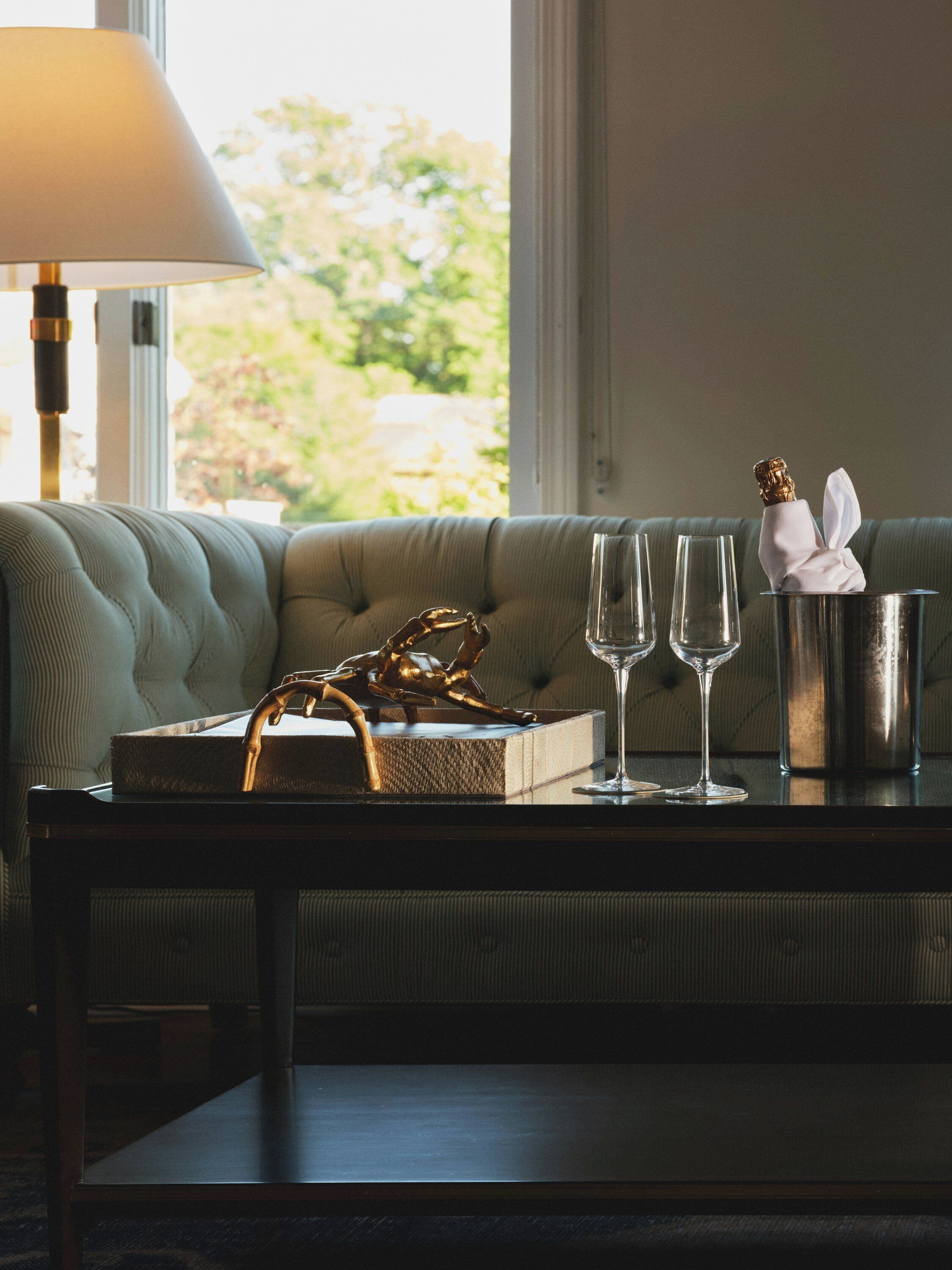 A sofa, a table with a lamp, two wine glasses, a gold sculpture, and a bottle of champagne.