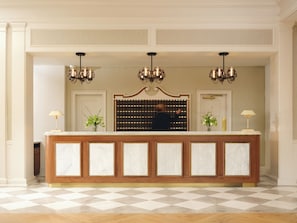 A reception area with a marble counter, two wall-mounted chandeliers, and a large decorative mirror above the counter.