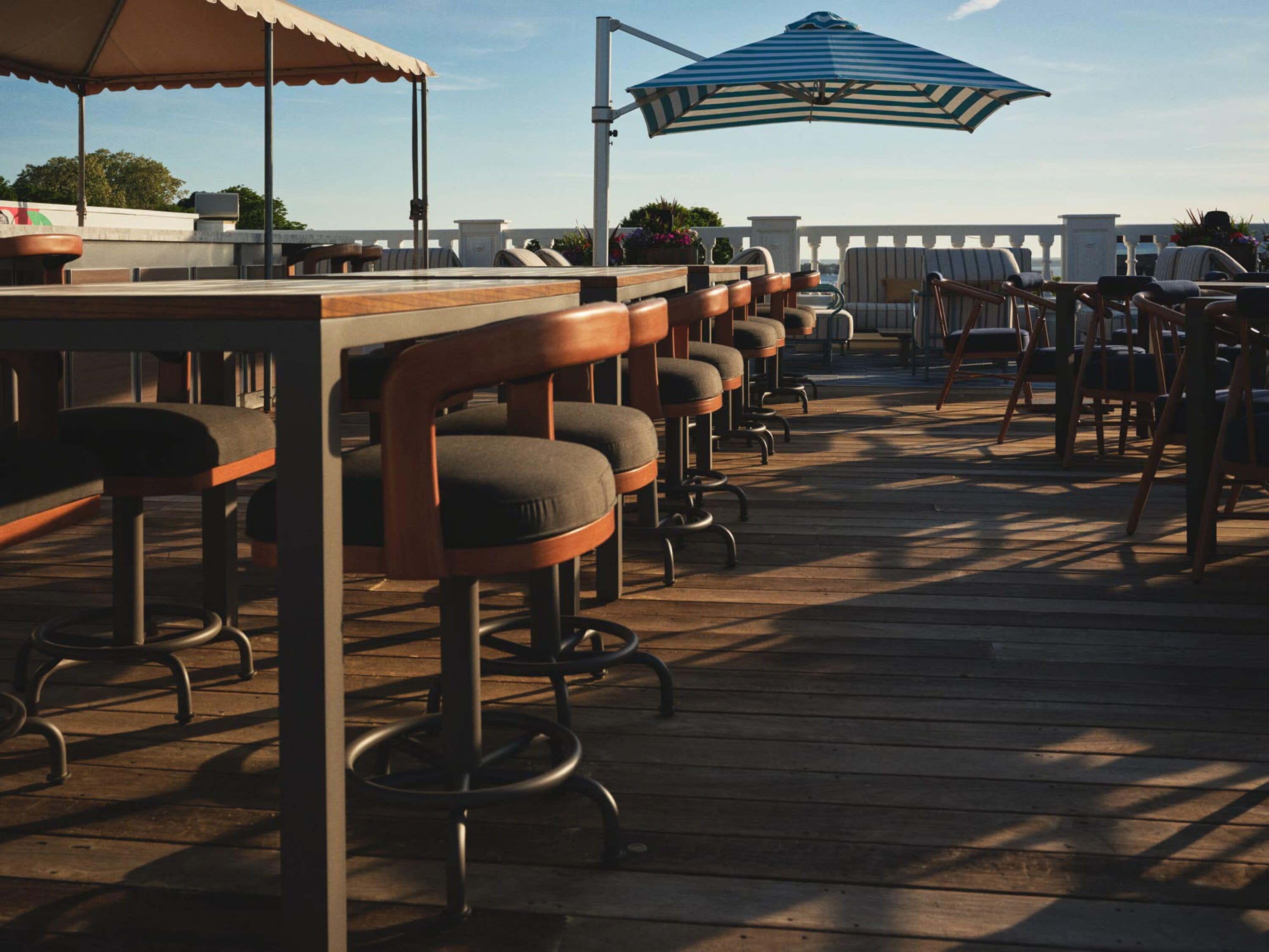 A bar area with multiple stools and tables, outdoor seating, and umbrellas providing shade.