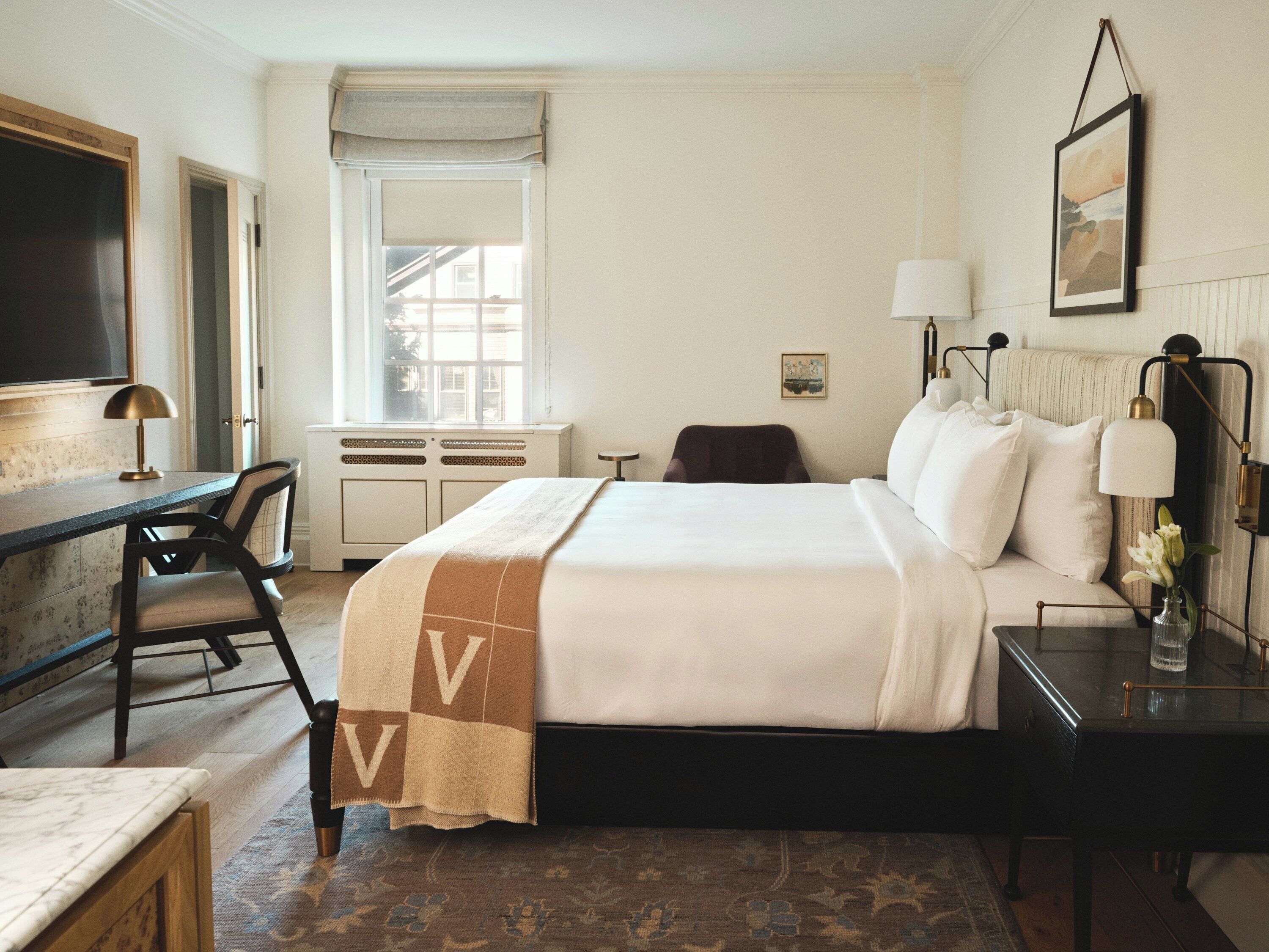 Habitación de hotel con cama, escritorio, silla, ventana y obras de arte.