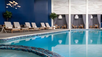 Un área de piscina interior moderna con sillones de descanso, piscina con azulejos y pared de mármol.
