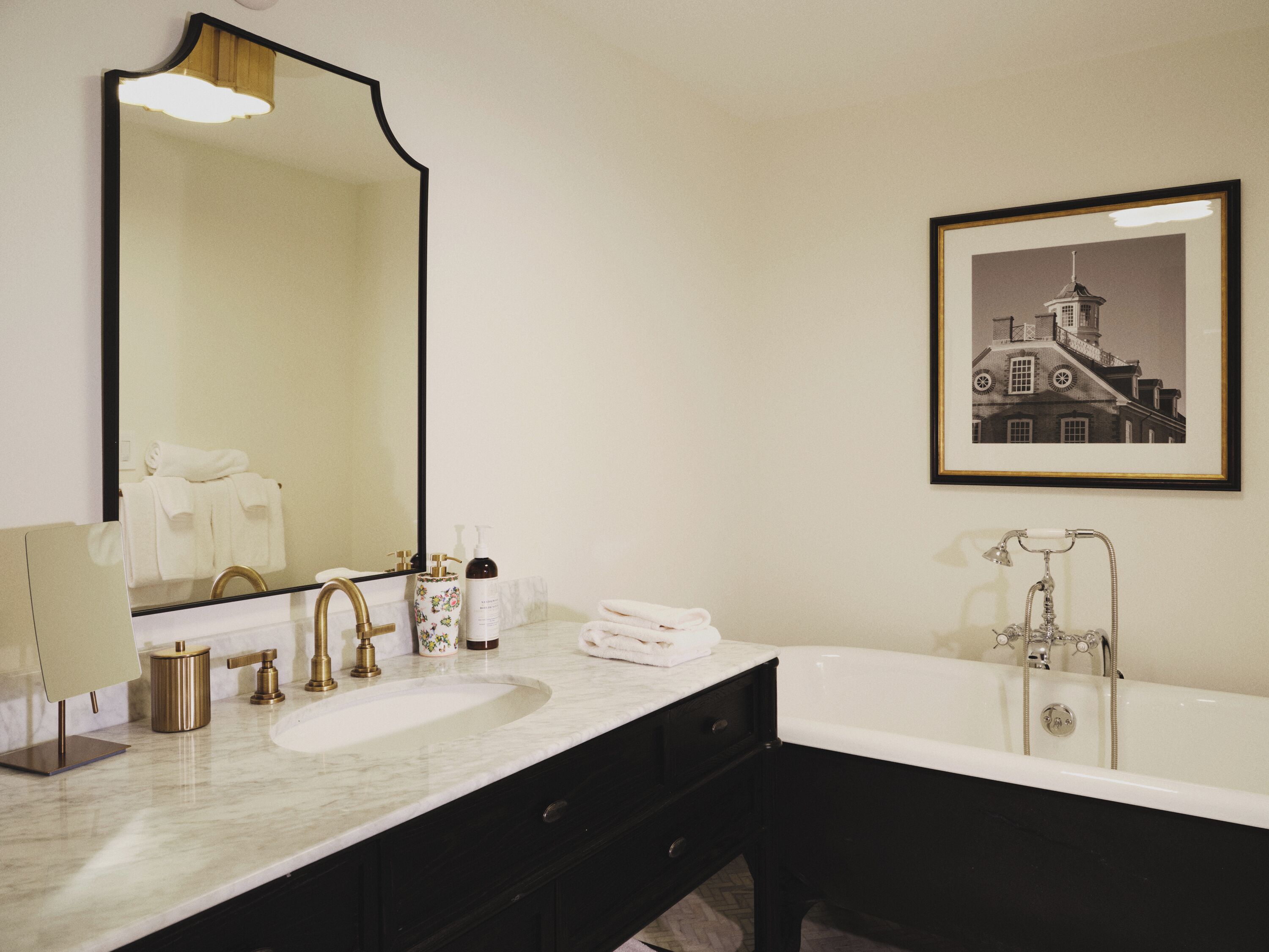 A bathroom with a large mirror, a sink, a bathtub, and a framed picture on the wall.
