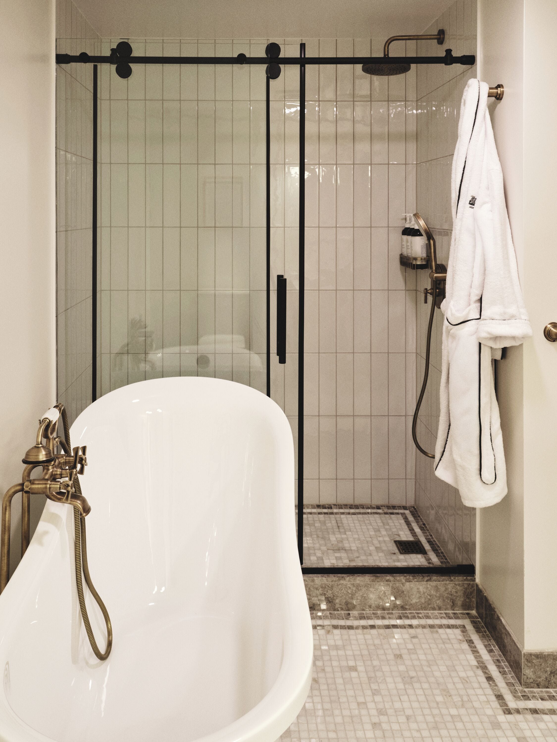 A bathroom with a white bathtub, a glass-enclosed shower, and a towel hanging on the wall.