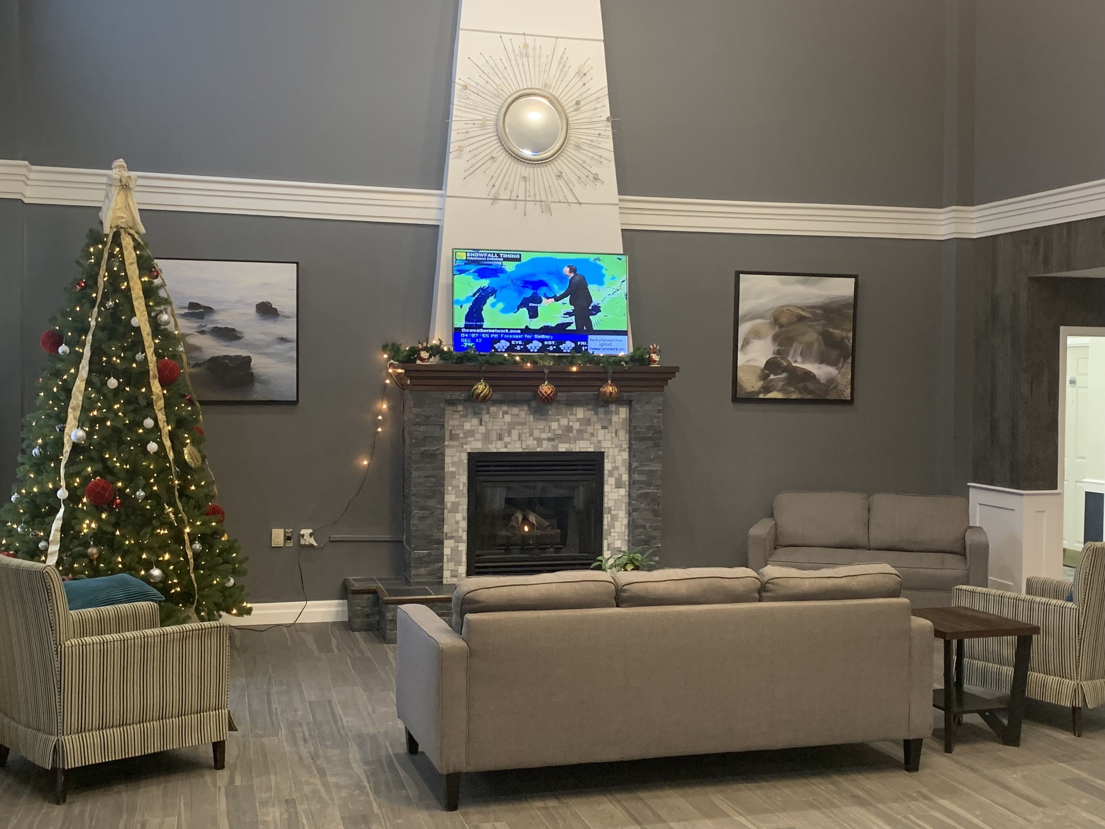 Una sala de estar con chimenea, un árbol de Navidad y un televisor mostrando un pronóstico del tiempo.