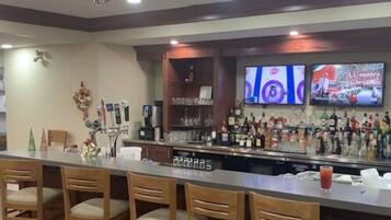 Zona de bar con taburetes de madera, barra con diversas botellas de licores y una pantalla de televisión que muestra un programa navideño.