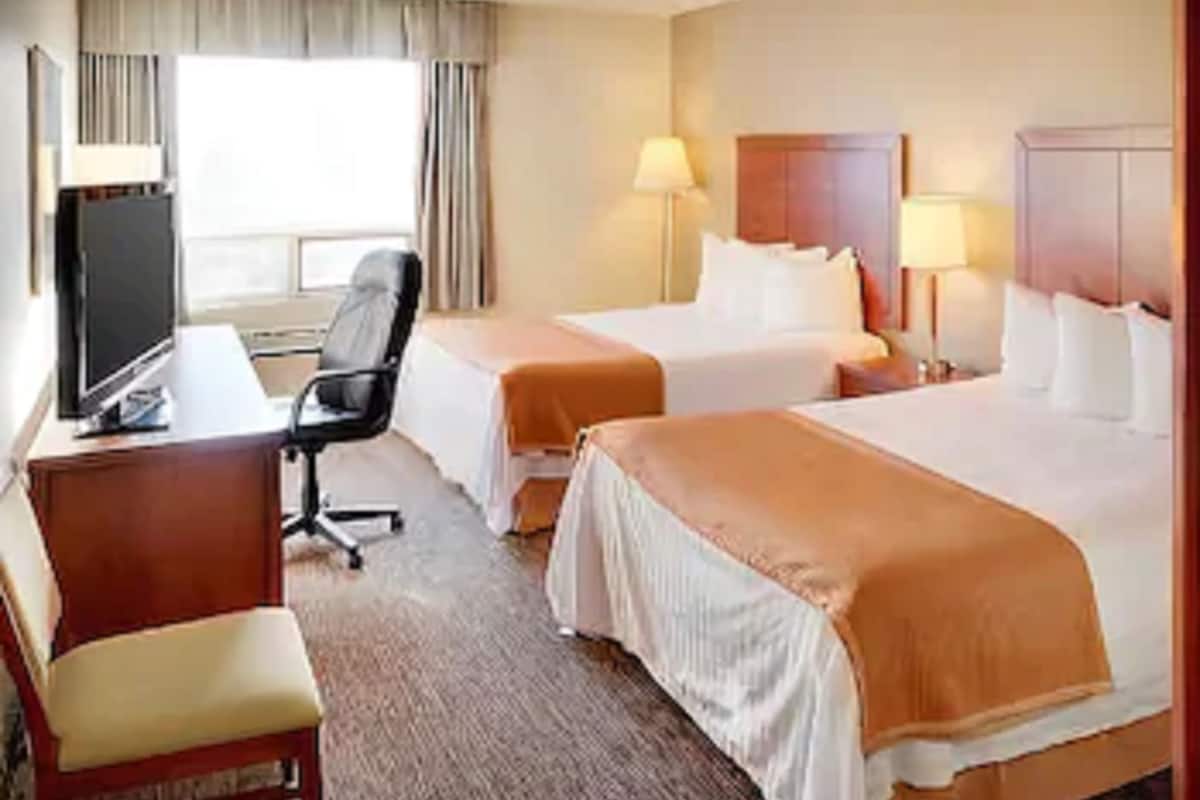 Ein Hotelzimmer mit zwei Betten, einem Schreibtisch mit Computer, einem Stuhl und einem Fernseher.