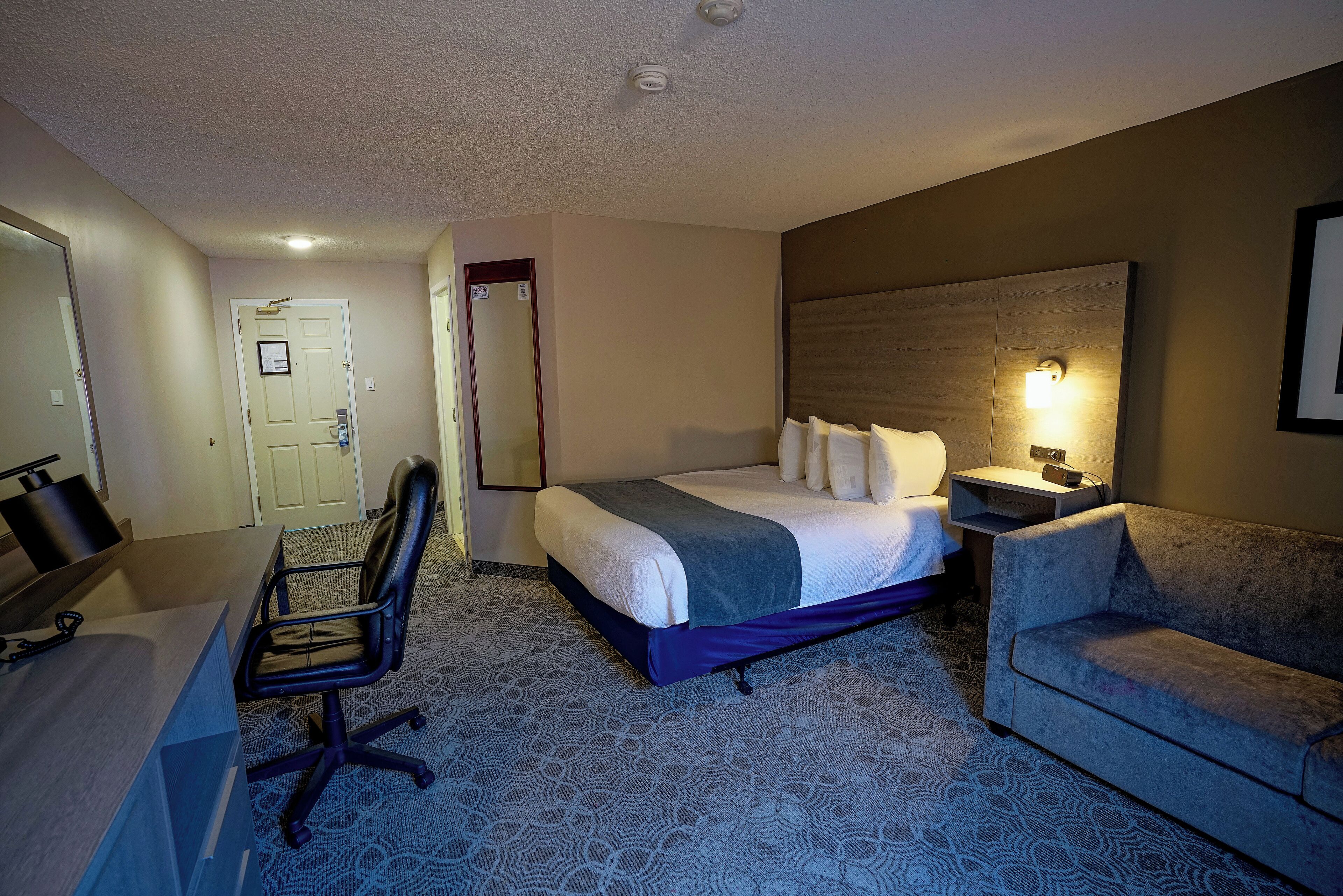 Quarto de hotel com cama, escrivaninha, cadeira e um sofá.