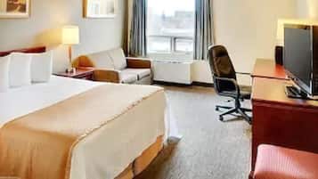 A hotel room with a large bed, a desk with a computer, a chair, a TV, and a window with curtains.