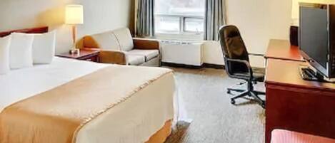 A hotel room with a large bed, a desk with a computer, a chair, a TV, and a window with curtains.