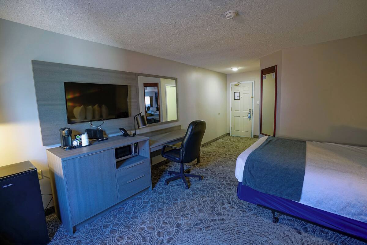 Ein Hotelzimmer mit einem Bett, einem Schreibtisch mit Stuhl, einem Fernseher und einem kleinen Kühlschrank.