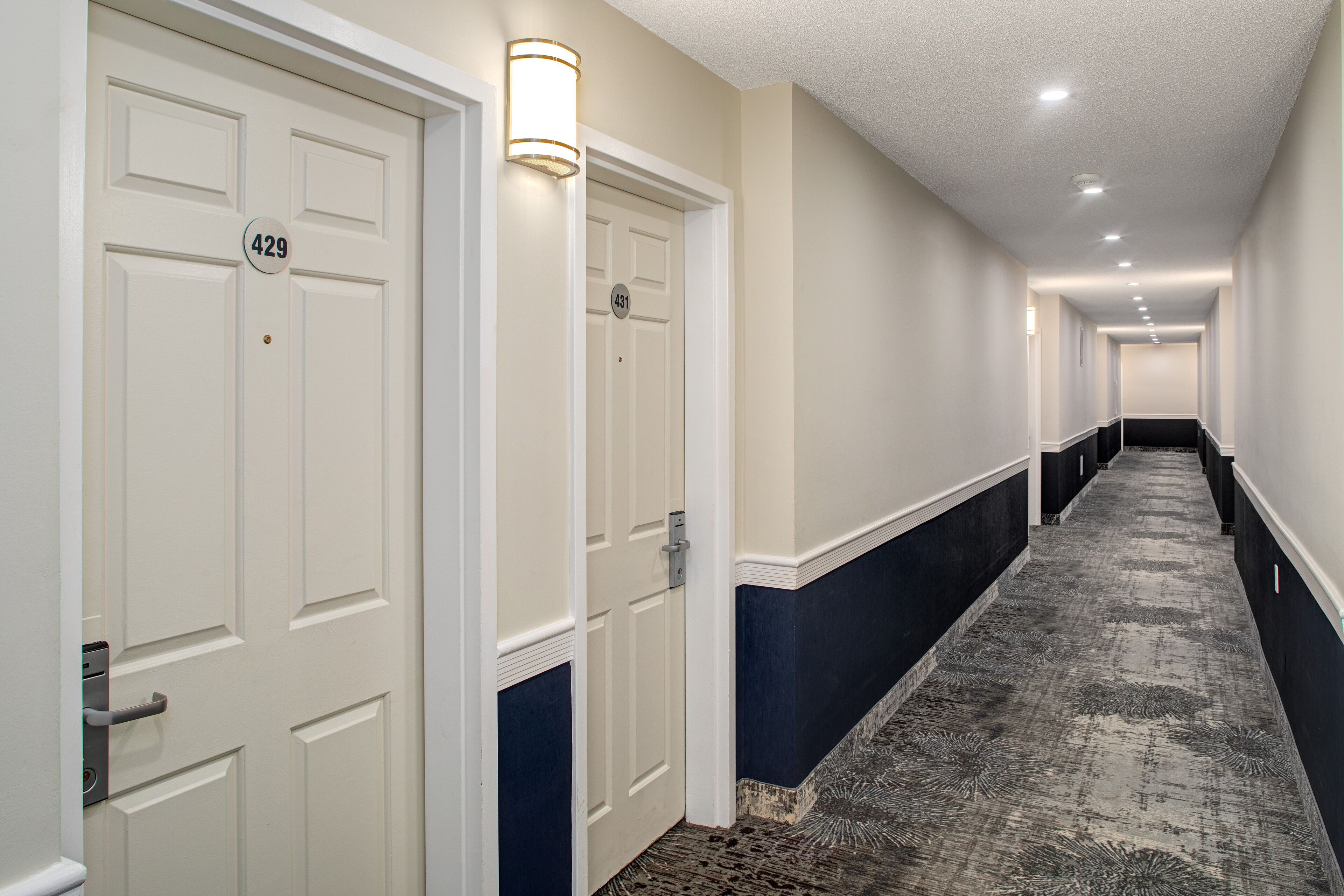 A hallway with doors numbered 429 and 431, a patterned carpet, and a light fixture on the wall.