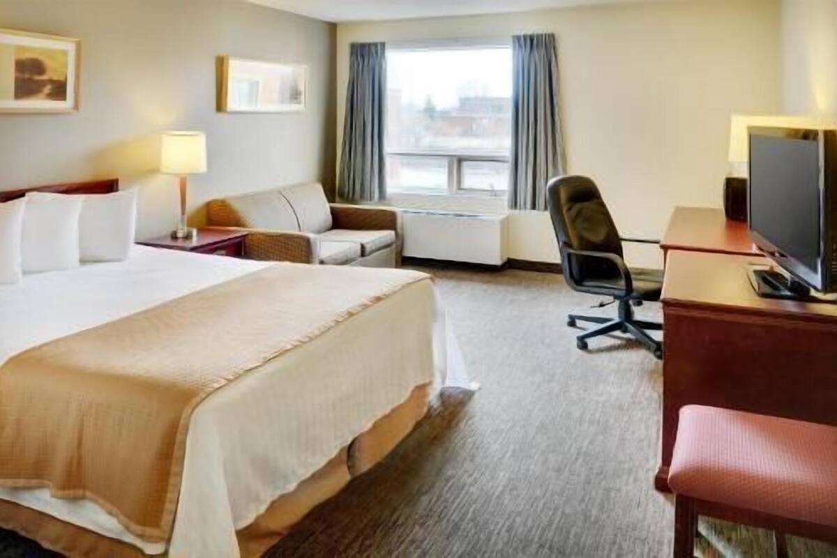 Ein Hotelzimmer mit Bett, Schreibtisch, Stuhl, Fernseher und einem Fenster mit Vorhängen.
