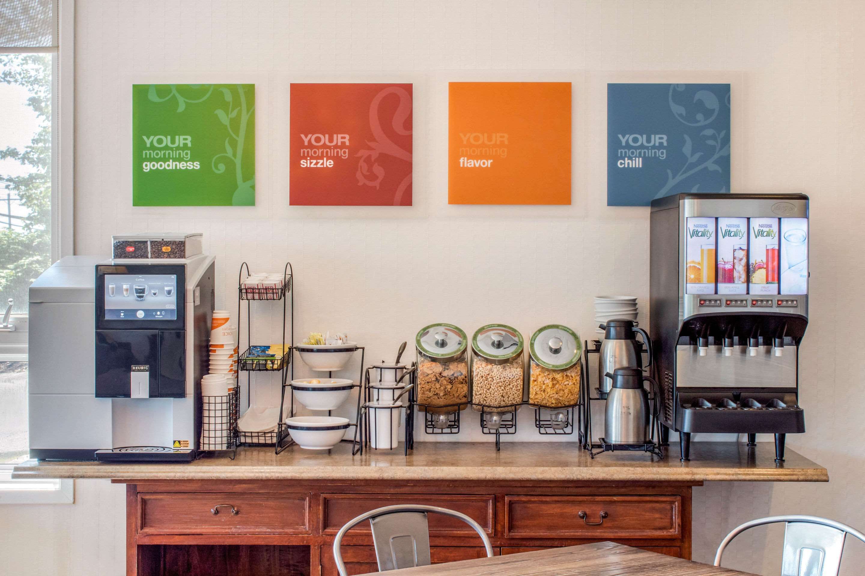 A breakfast bar with a coffee machine, tea dispensers, and a coffee press. There are four framed signs on the wall with motivational phrases.