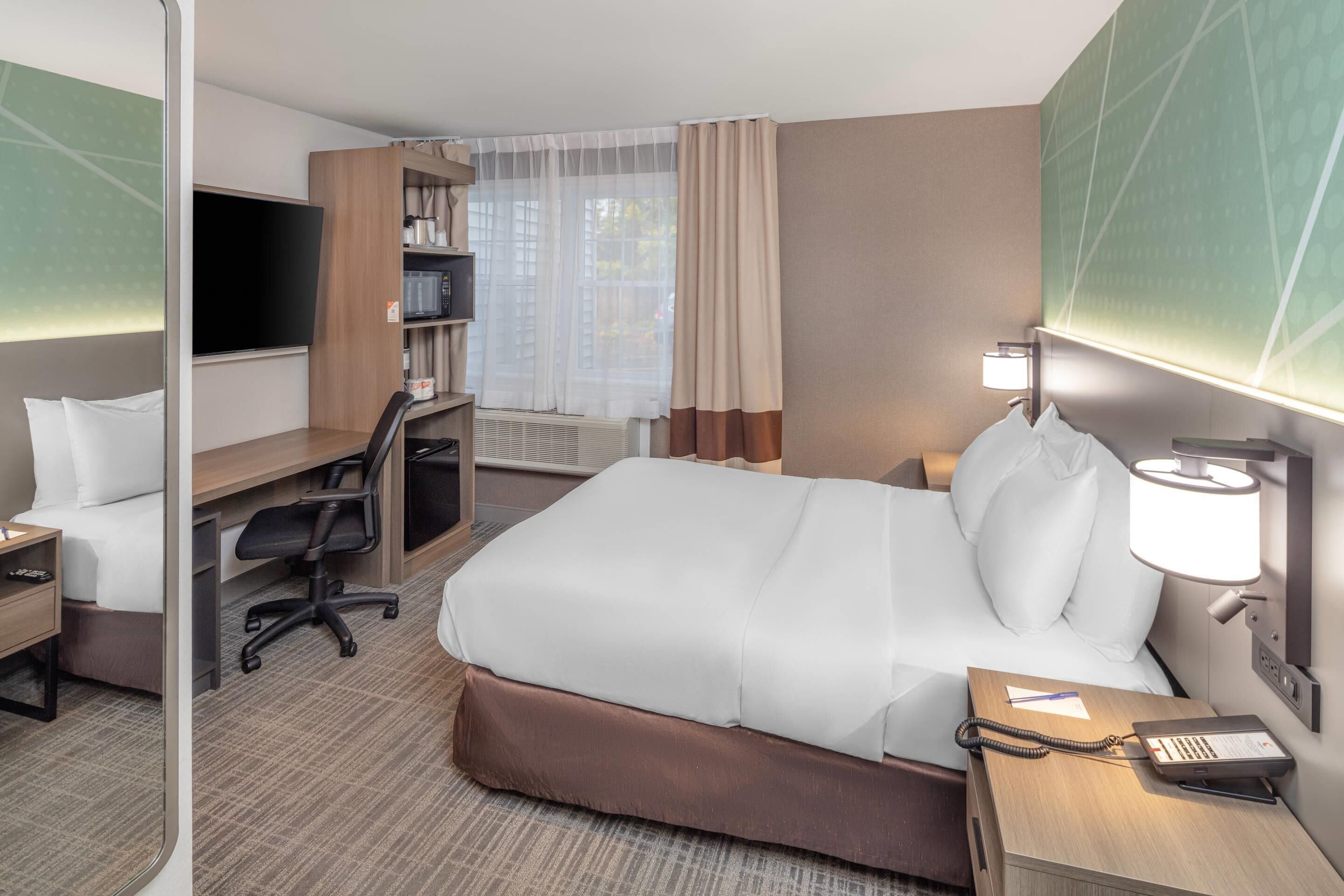 A hotel room with a bed, desk, chair, TV, and a bedside lamp.