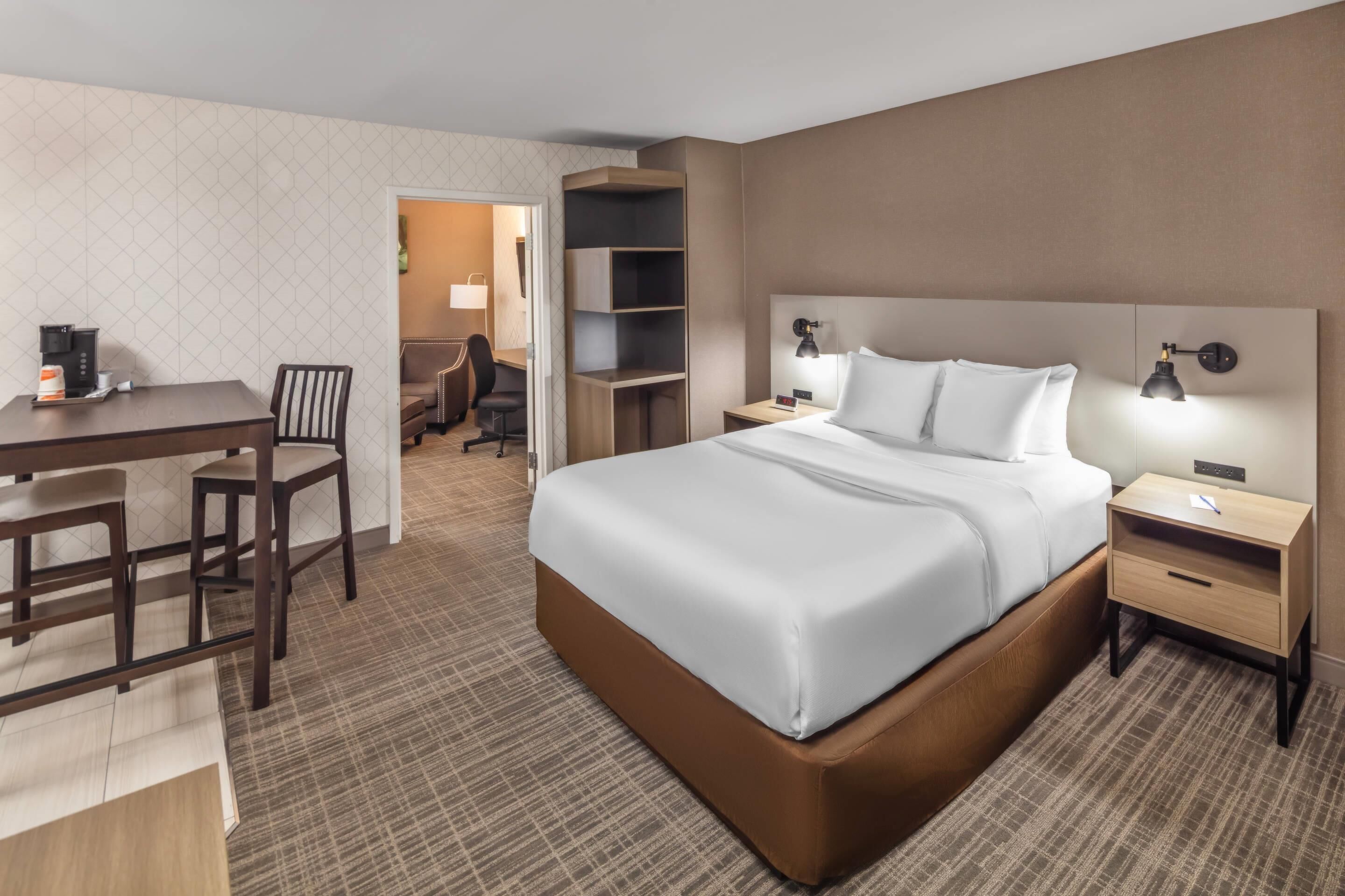 Ein Hotelzimmer mit einem großen Bett, einem Schreibtisch mit Stuhl, einem Kleiderschrank und einem Nachttisch mit Lampen.