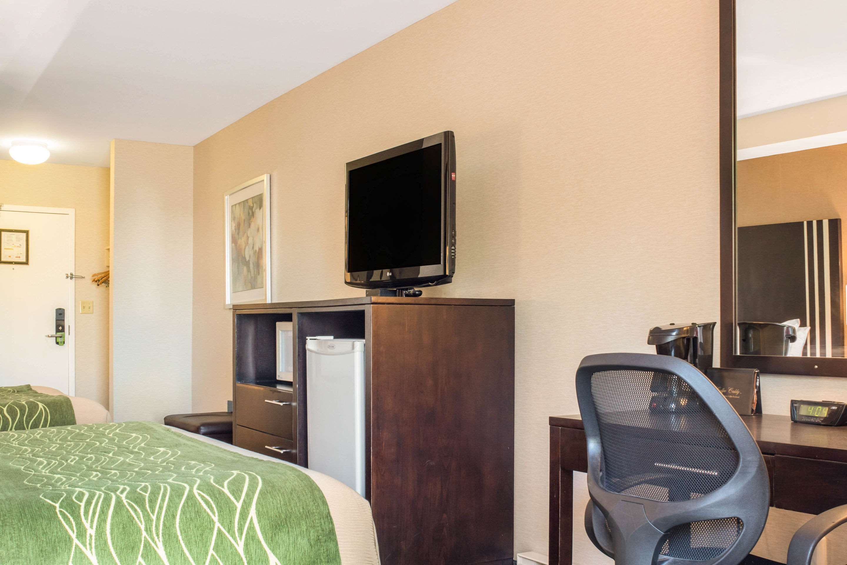 A hotel room with a bed, a desk with a computer, a chair, a television, and a refrigerator.