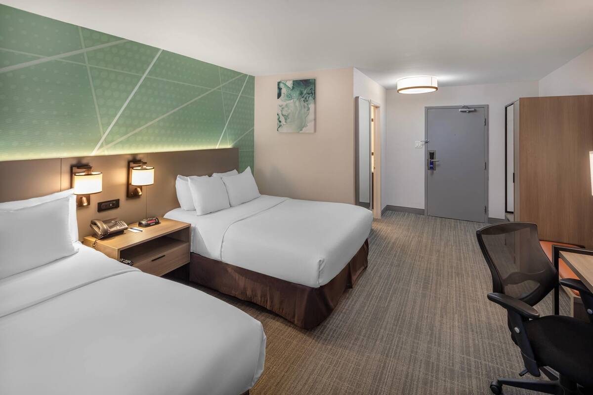 Une chambre d’hôtel avec deux lits, un bureau, une chaise et un mur d’accent vert.