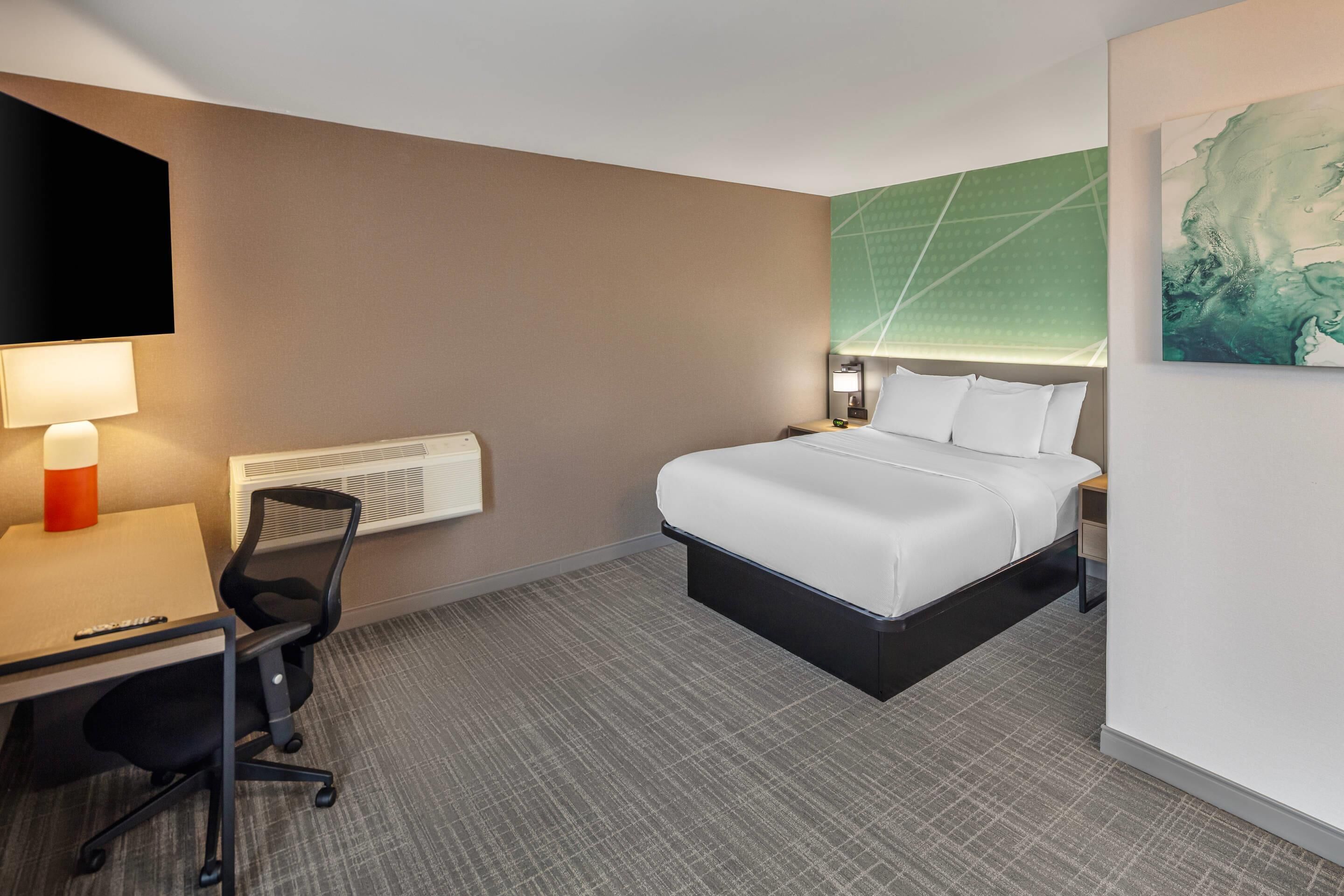 Een hotelkamer met een bed, bureau, stoel en een groot schilderij aan de muur.