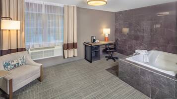 Habitación de hotel con sofá, escritorio, silla y una bañera grande.
