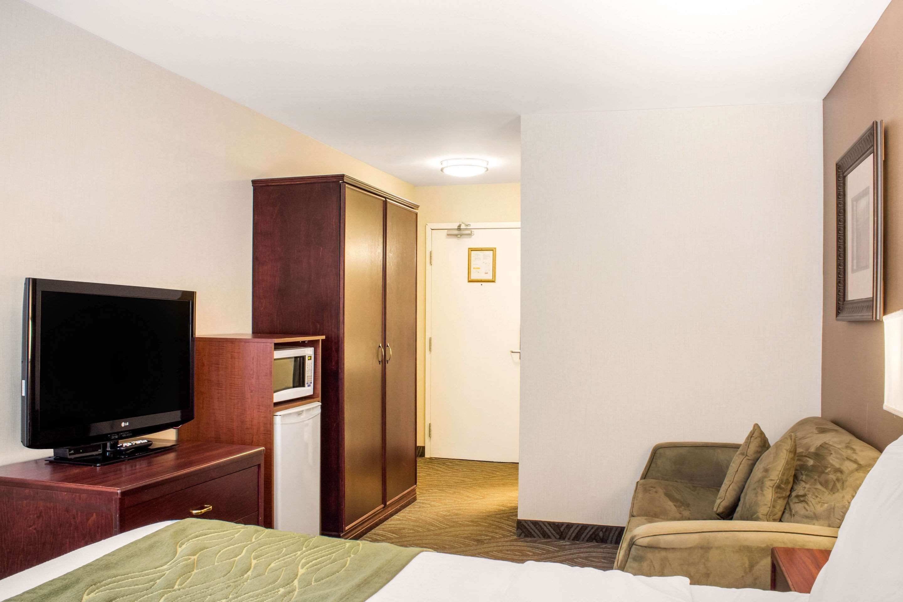 Habitación de hotel con cama, televisión sobre un aparador de madera, armario, microondas y sofá.