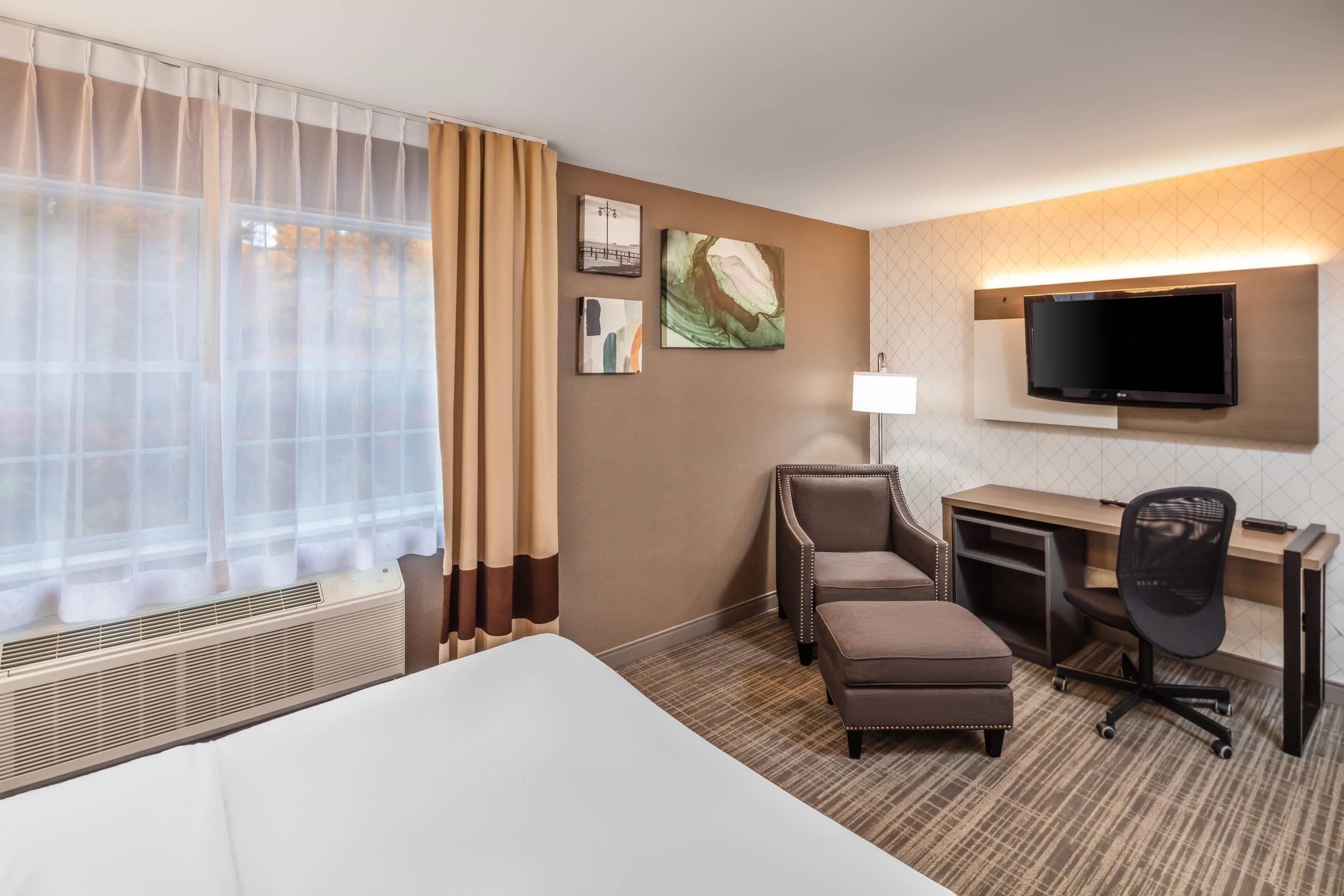 Une chambre d’hôtel avec un lit, un bureau, une chaise, une télévision et des œuvres d’art accrochées au mur.