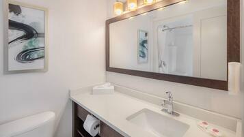 A bathroom with a white sink, a mirror with lights, a toilet, and a towel dispenser.