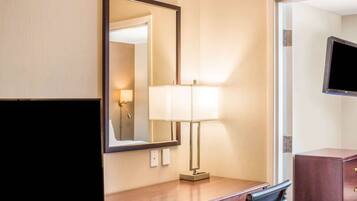 Una habitación de hotel con un escritorio de madera, un espejo, una lámpara, un televisor y un armario.