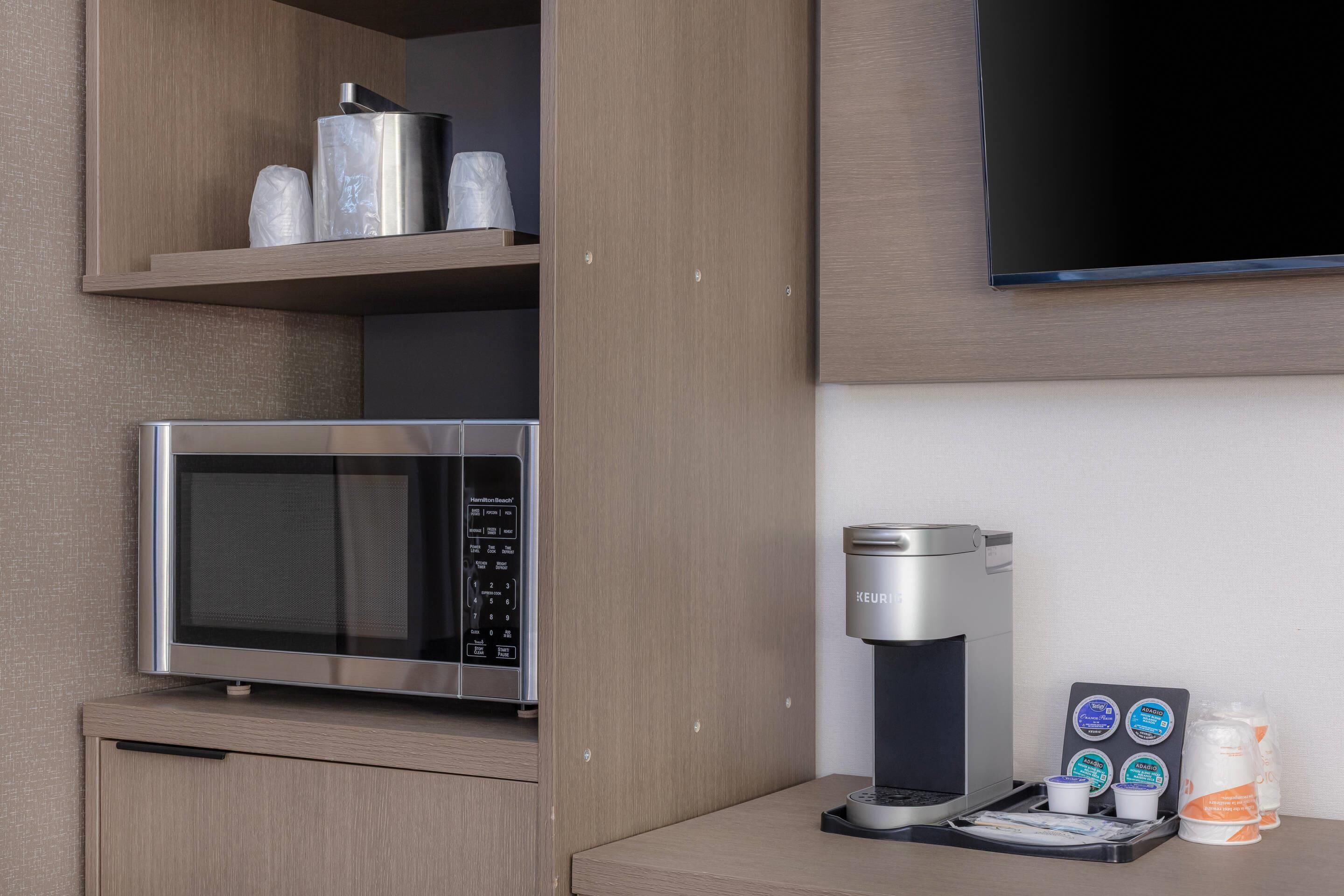 Una kitchenette con microondas, cafetera y cápsulas de café.