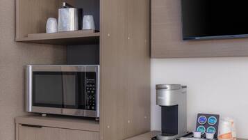 Una kitchenette con microondas, cafetera y cápsulas de café.