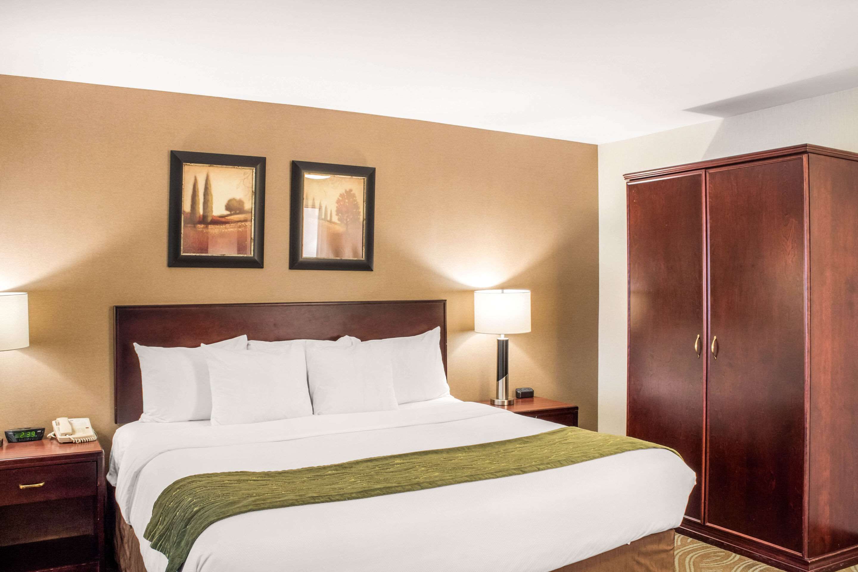 A hotel room with a large bed, two bedside lamps, a wooden wardrobe, and two framed pictures on the wall.