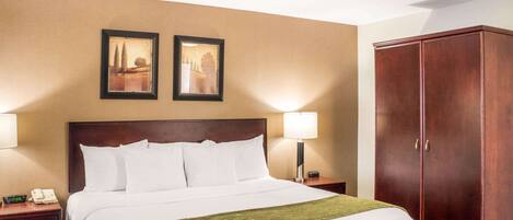 A hotel room with a large bed, two bedside lamps, a wooden wardrobe, and two framed pictures on the wall.