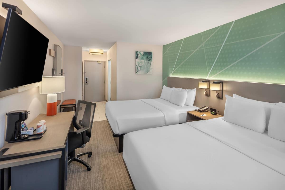 Une chambre d’hôtel avec deux lits, un bureau doté d’une machine à café, une télévision et une porte donnant accès à une salle de bain.