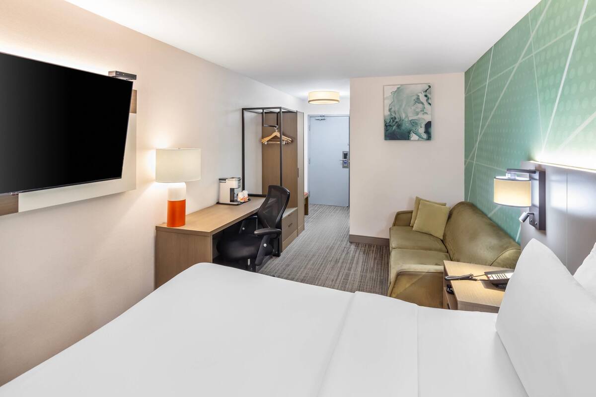 Une chambre d’hôtel comprenant un lit, un bureau avec une chaise, un canapé, une t élévision, une lampe et un tableau au mur.