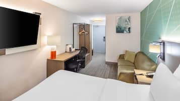 Una camera d'albergo con un letto, una scrivania con una sedia, un divano, una televisione, una lampada e un quadro appeso al muro.