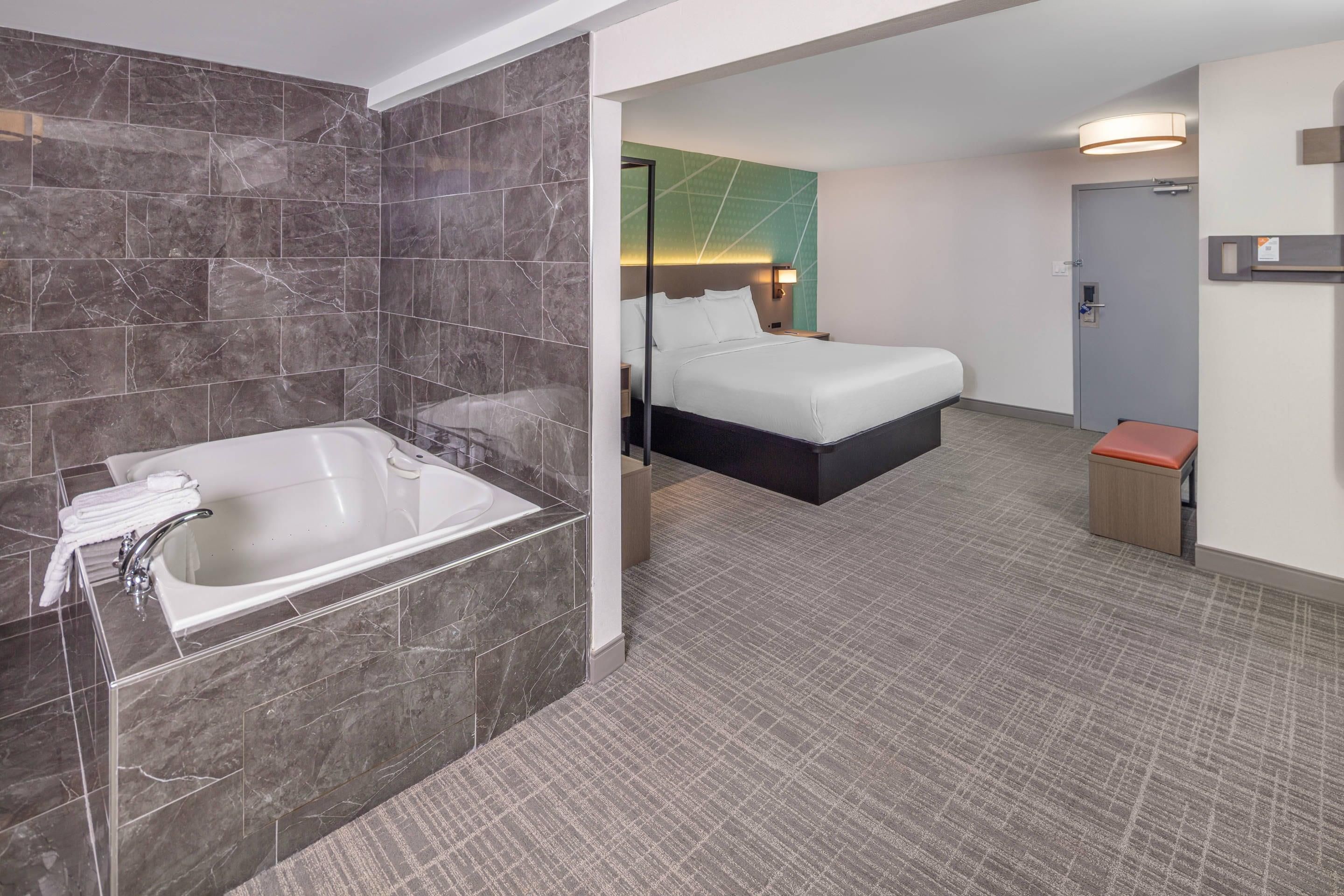 A hotel room with a marble-tiled bathroom, a bed with white linens, and a small seating area.