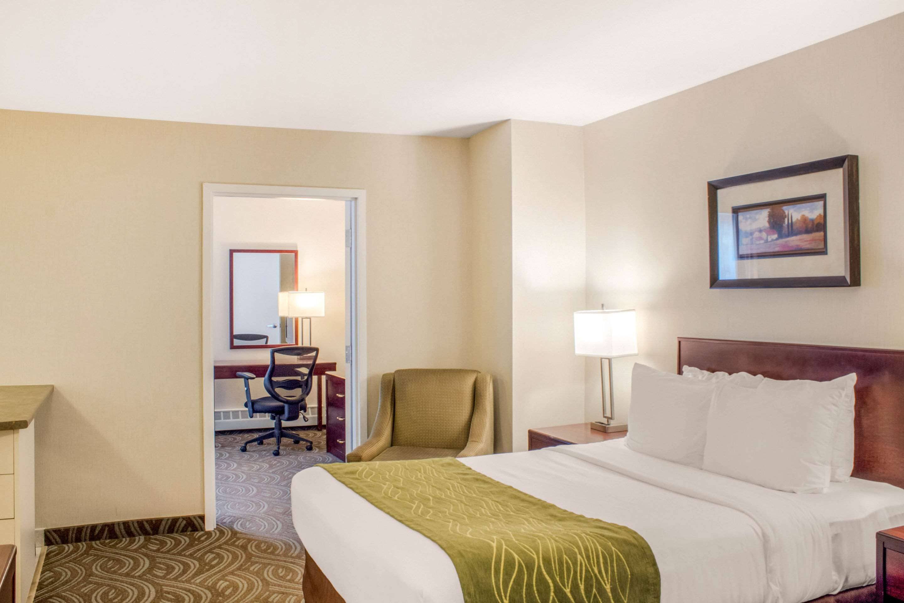 A hotel room with a bed, a desk, a chair, a lamp, and a framed picture on the wall.