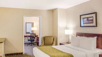A hotel room with a bed, a desk, a chair, a lamp, and a framed picture on the wall.