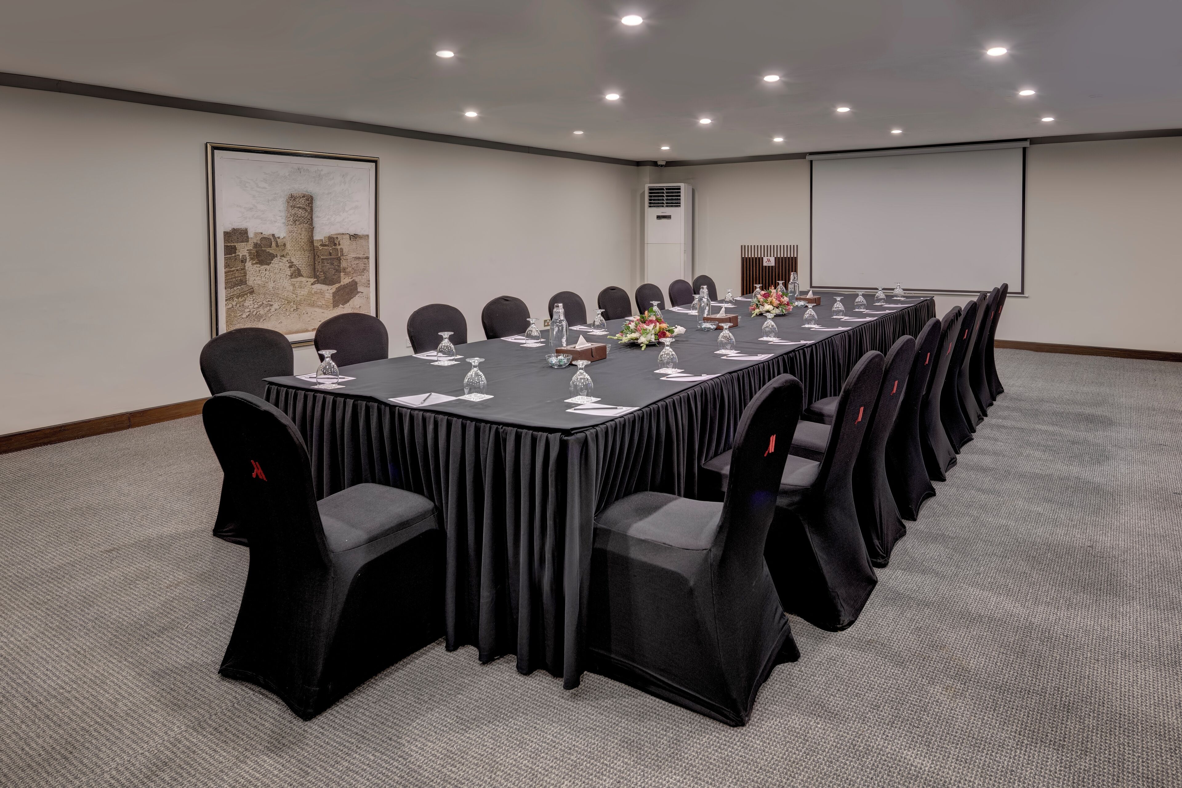 Ein Konferenzraum mit einem langen Tisch, schwarzen Stühlen und einer Projektionsleinwand.