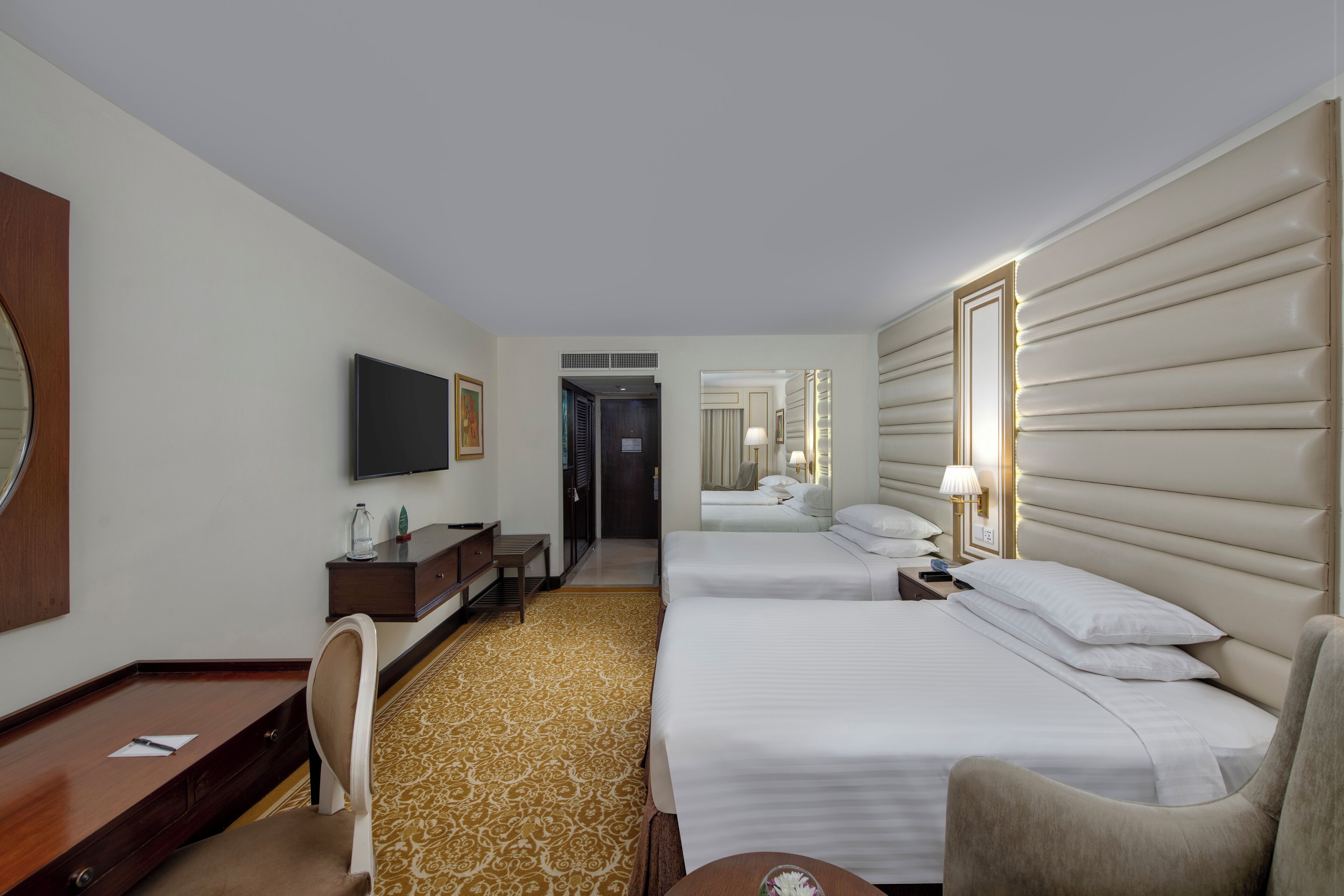 A hotel room with a bed, a desk, a chair, a TV, and a mirror.