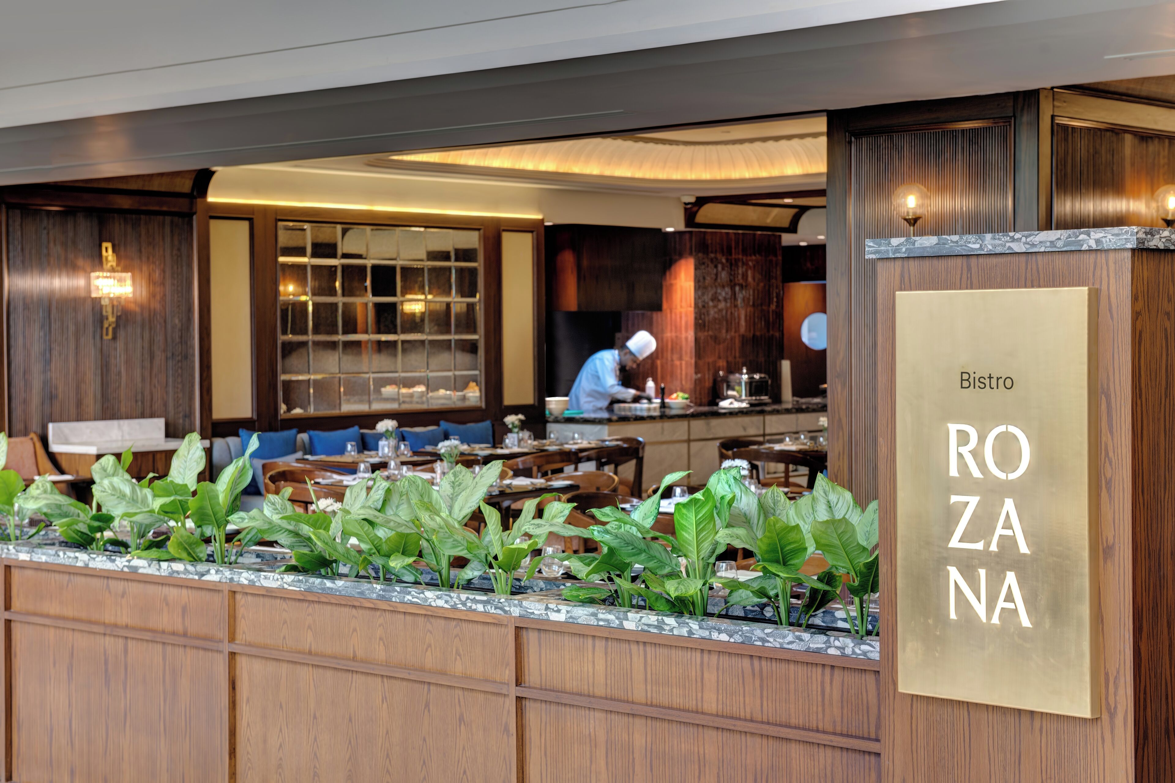 A restaurant interior with wooden paneling, a chef preparing food, and a sign reading "Bistro ROZANA".