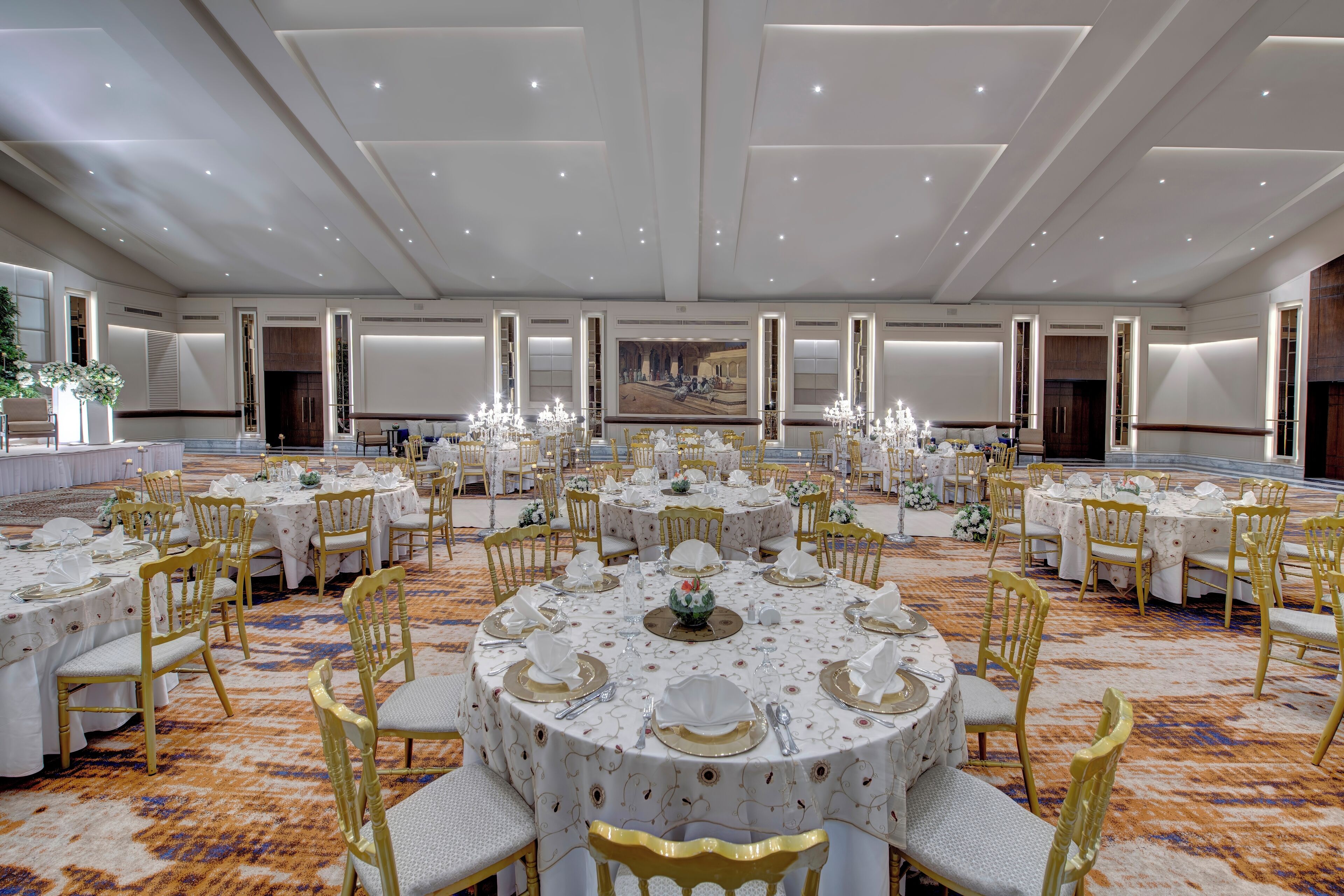 Une vaste salle de banquet avec des tables rondes dressées pour le repas, agrémentée de chaises dorées et de nappes blanches.