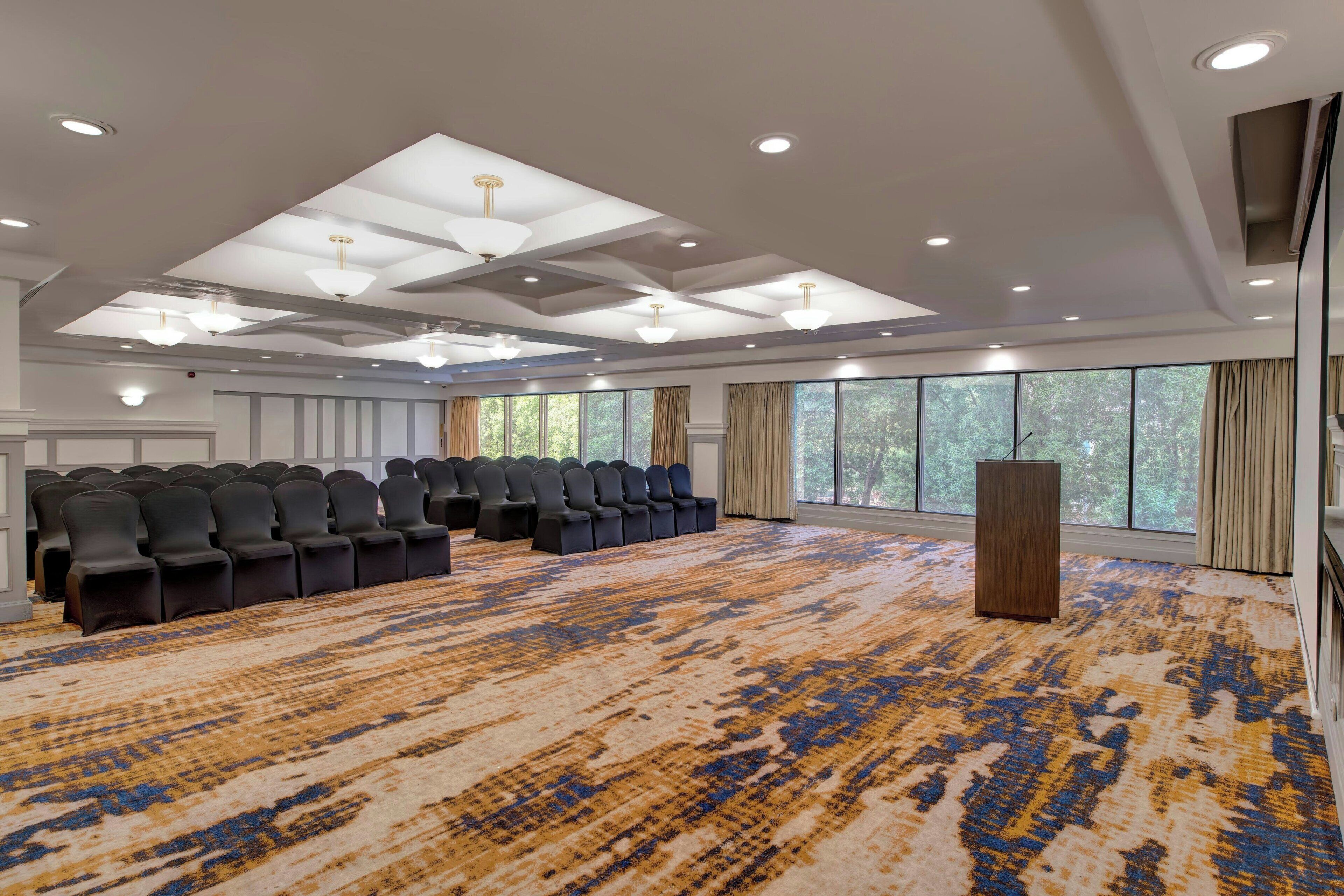 Un salón de conferencias con filas de sillas, un atril y ventanas amplias.