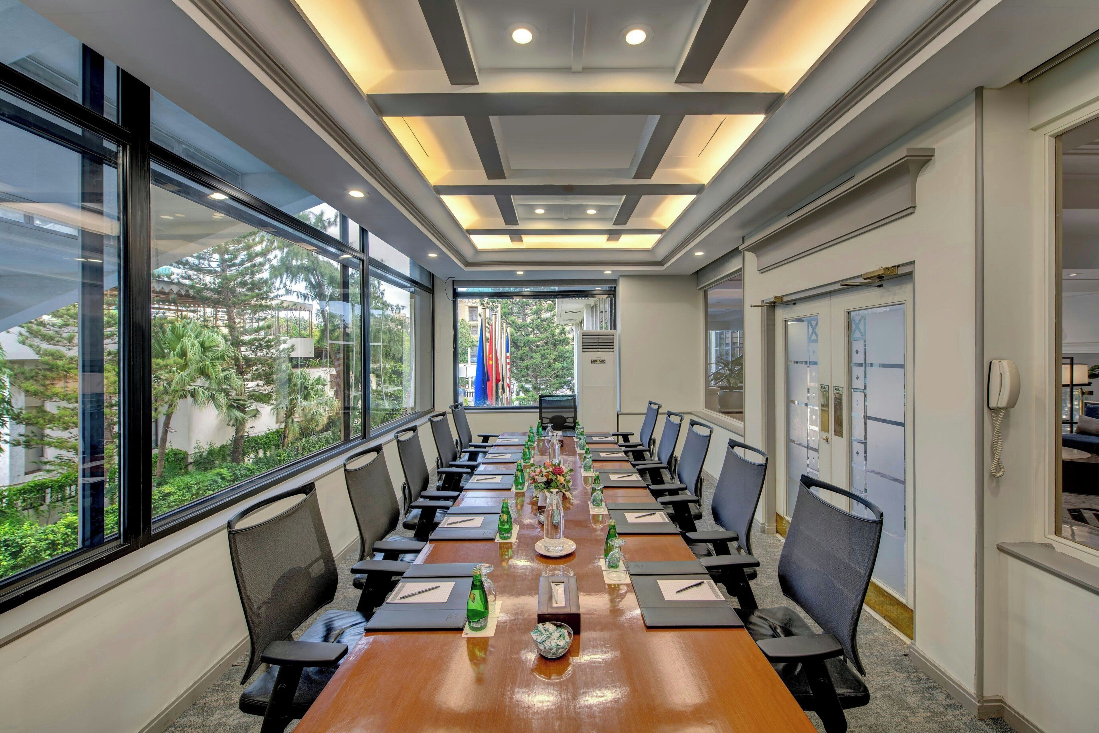 A conference room with a long table, chairs, and a view through large windows.