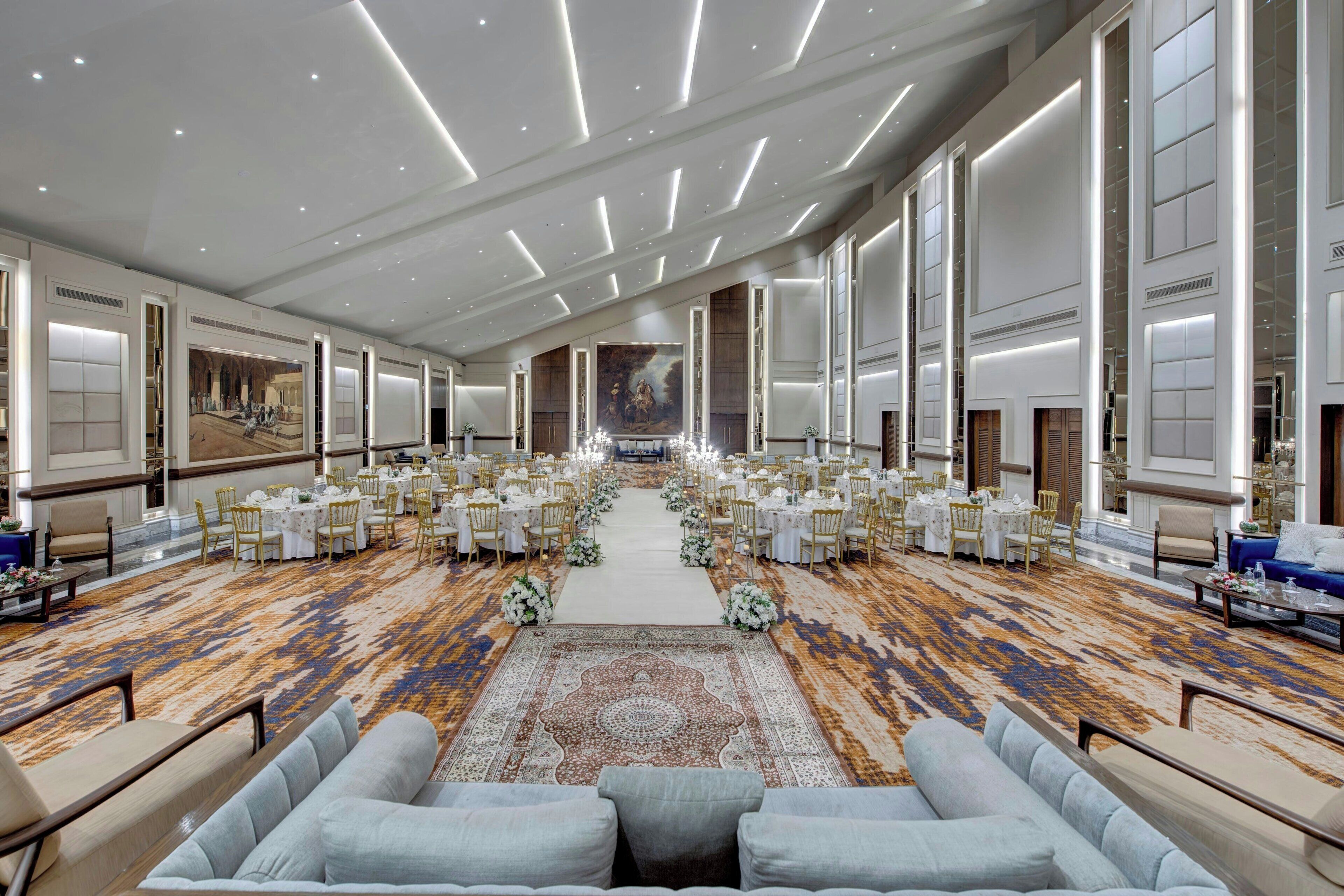 A spacious hotel lobby with a central aisle, rows of tables and chairs, and a patterned carpet.