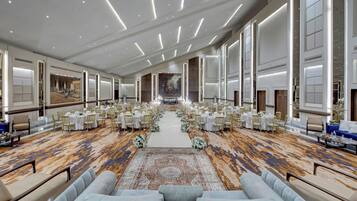 A spacious hotel lobby with a central aisle, rows of tables and chairs, and a patterned carpet.