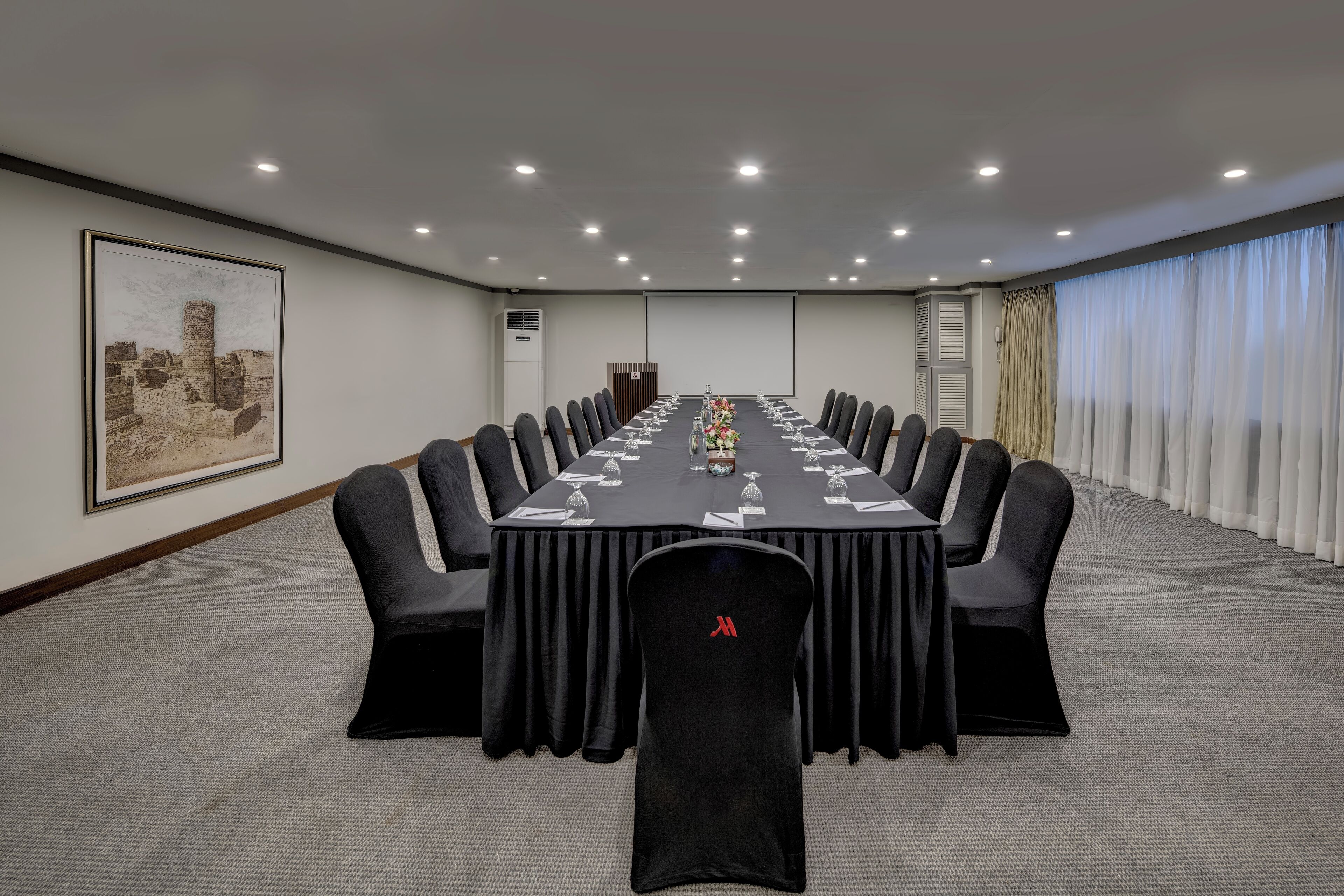 Ein Konferenzraum mit einem langen Tisch, schwarzen Stühlen und einer Projektionsleinwand.