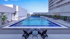 Una piscina en la azotea con una mesa y sillas, rodeada de sillones de descanso y una barandilla.