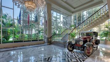 Un lobby elegante con un coche clásico, un candelabro y una escalera que sube a plantas superiores.