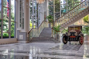 A grand staircase with a vintage car at the base, surrounded by large windows and indoor plants. - Marriott Karachi Hotel (Karachi)